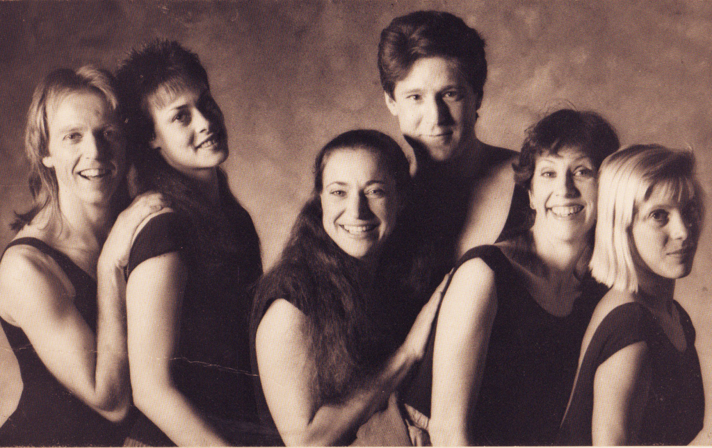 An black & white image of 6 individuals smile and look at the camera wearing dance clothes.